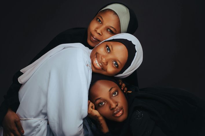 Three women in hijabs smiling and embracing, showcasing unity and tradition.